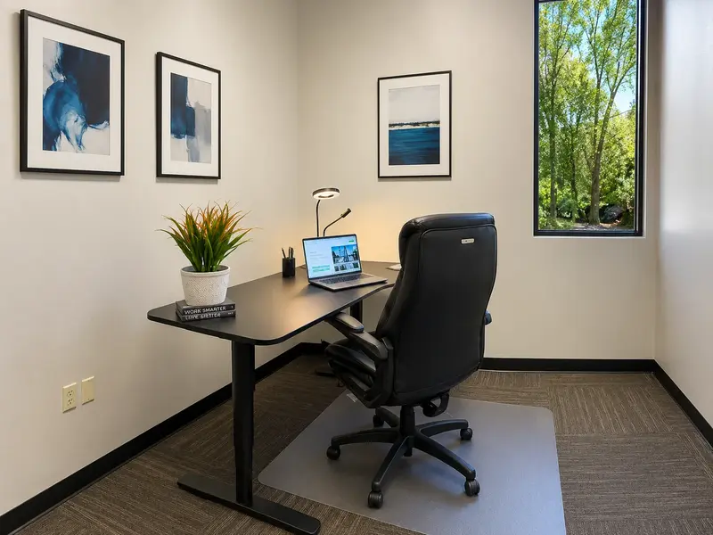 Private executive office Suite 113 with an electric sit-stand desk, ergonomic chair, and natural light from a window.