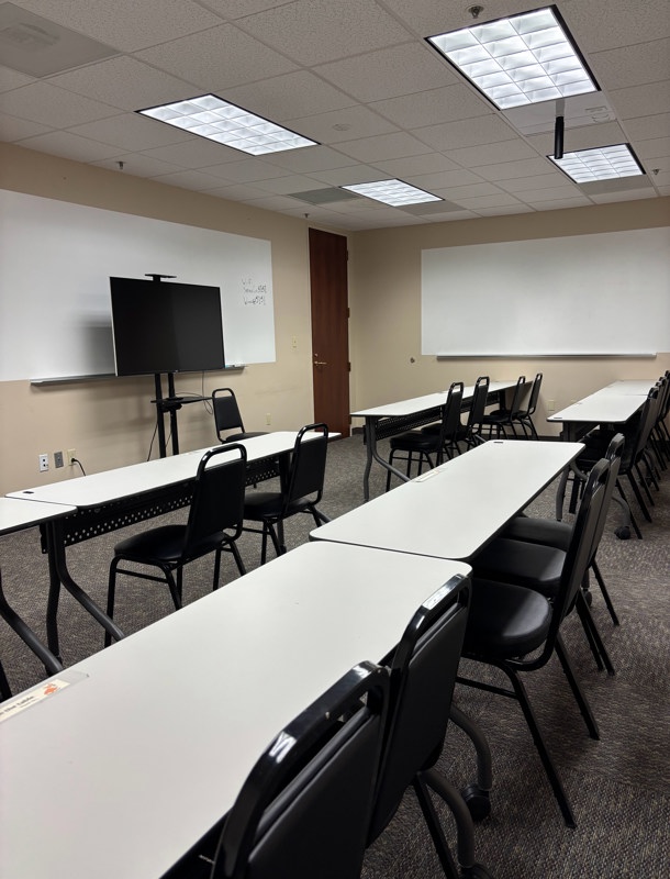 Professional classroom setup in Suite 690 with rows of desks, chairs, whiteboards, and a large TV for presentations.
