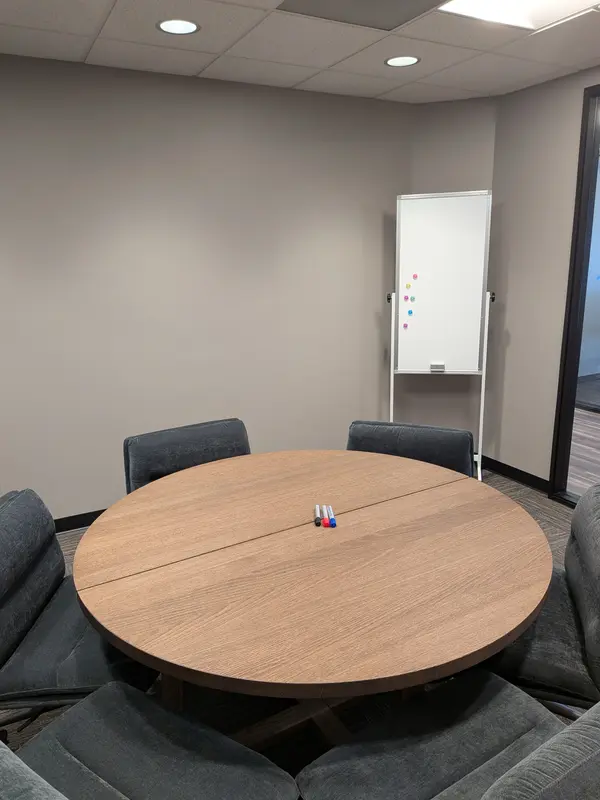 The Conference Lounge features a round wooden table, plush grey chairs, and a mobile whiteboard for team collaboration.