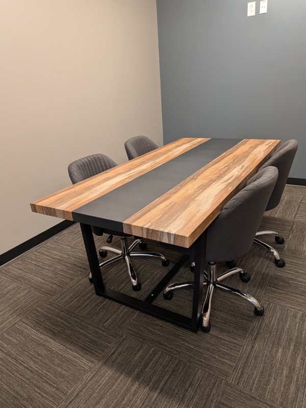 Small meeting room 'The Think Tank' with a modern wood-grain table and four gray office chairs for team collaboration.