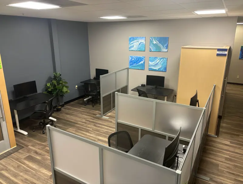 Individual drop-in workstations with frosted glass dividers and ergonomic chairs at Spoke Coworking.