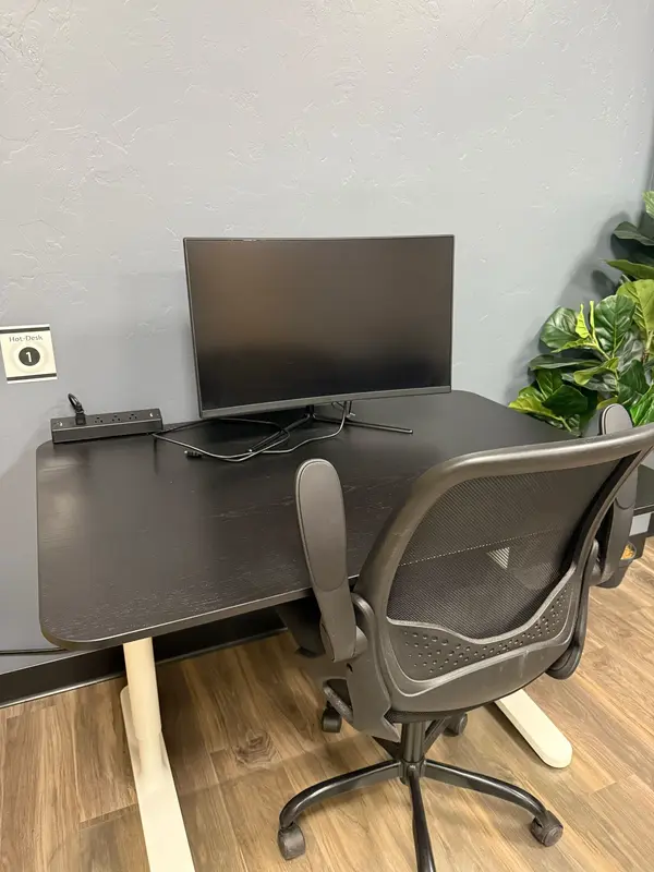 Hot Desk 1 in a Tucson coworking space with a black desk, ergonomic chair, and large computer monitor.