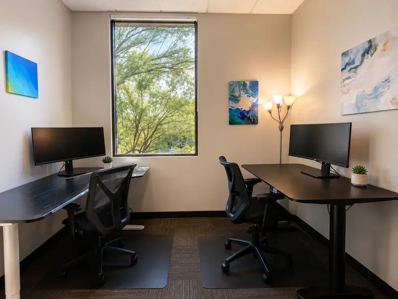 Private junior office Suite 111 at Spoke Coworking featuring two sit-stand desks, curved monitors, and a window.