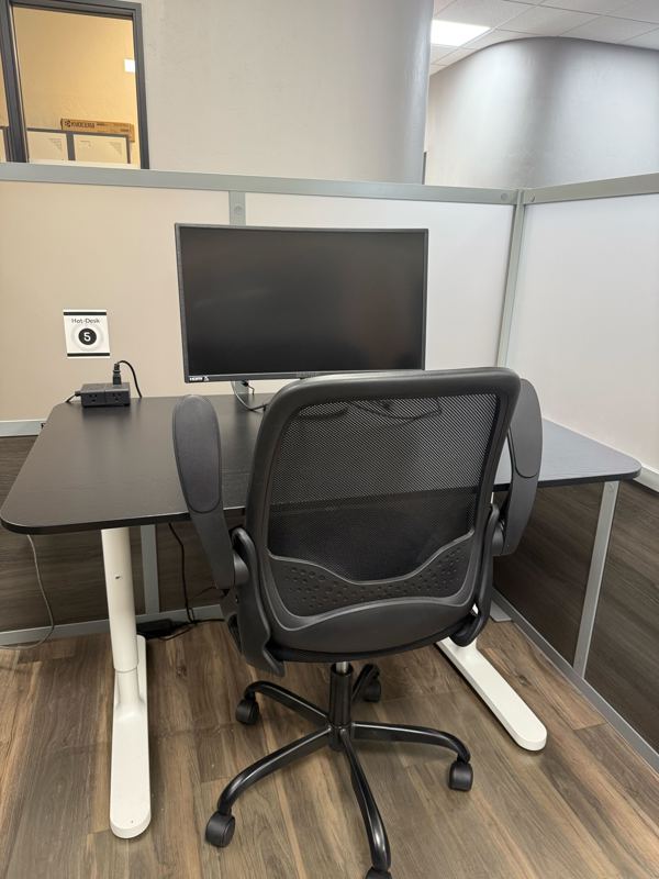 Semi-private Hot Desk 5 in a Tucson coworking space with a large monitor, ergonomic chair, and privacy partitions.