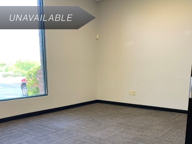 Empty private team office Suite 101 with a large window and grey carpet tiles, currently marked as unavailable.