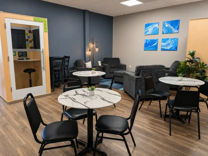 Cafe workspace area at Spoke Coworking featuring marble round tables, comfortable armchairs, and a private phone booth.