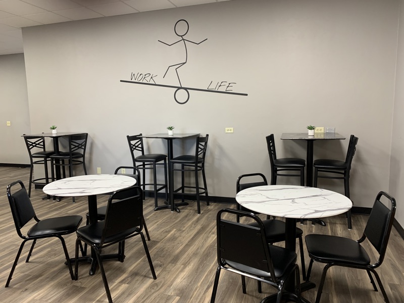 Cafe seating area at a Tucson coworking space with marble tables and a work-life balance wall decal.