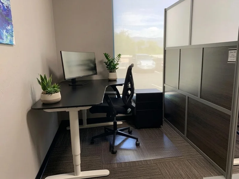 Dedicated Desk 205 featuring an electric sit-stand desk, curved monitor, and mountain views in a semi-private workspace.
