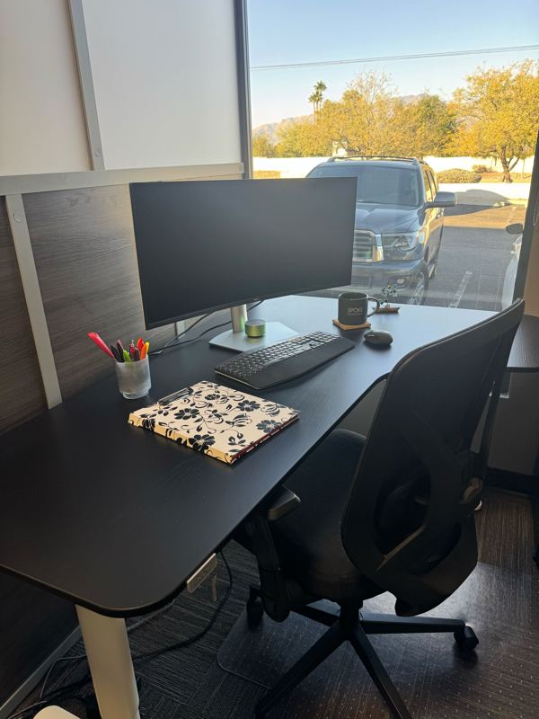 Semi-private dedicated desk at Spoke Coworking with a curved monitor, sit-stand desk, and scenic mountain views.