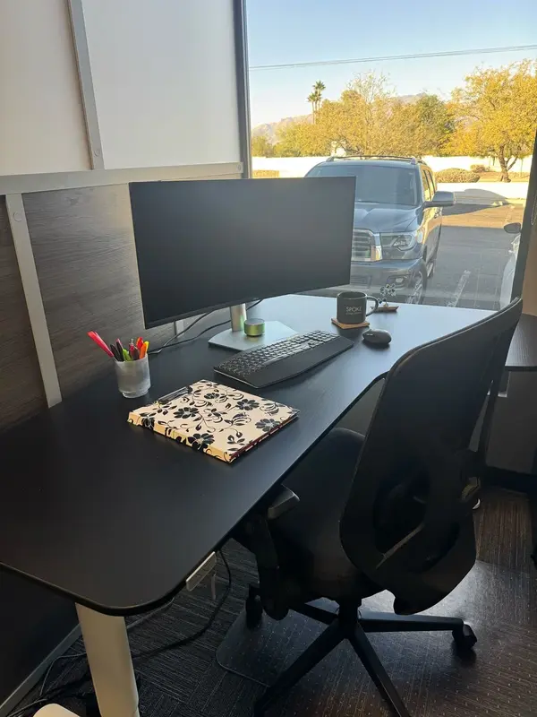 A semi-private dedicated desk at Spoke Coworking with a curved monitor, sit-stand desk, and scenic mountain views.