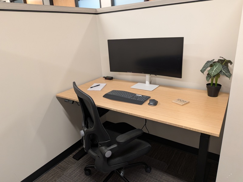 A semi-private dedicated desk with a bamboo sit-stand desk and ergonomic mesh chair at Spoke Coworking in Tucson.