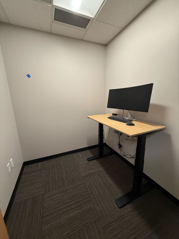 Private Suite 129 micro office featuring an electric sit-stand bamboo desk and a large curved monitor.
