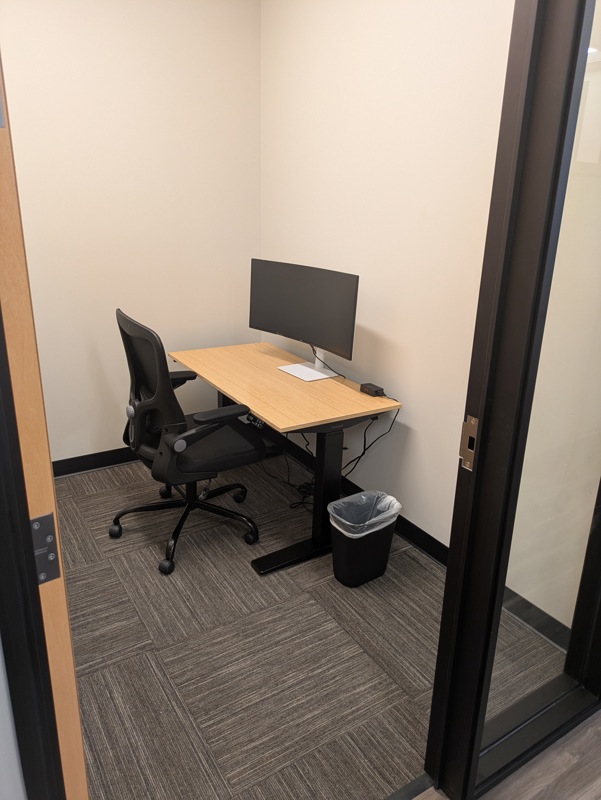 Private Micro Suite 135 with a bamboo sit-stand desk and curved monitor for focused work in a lockable office.