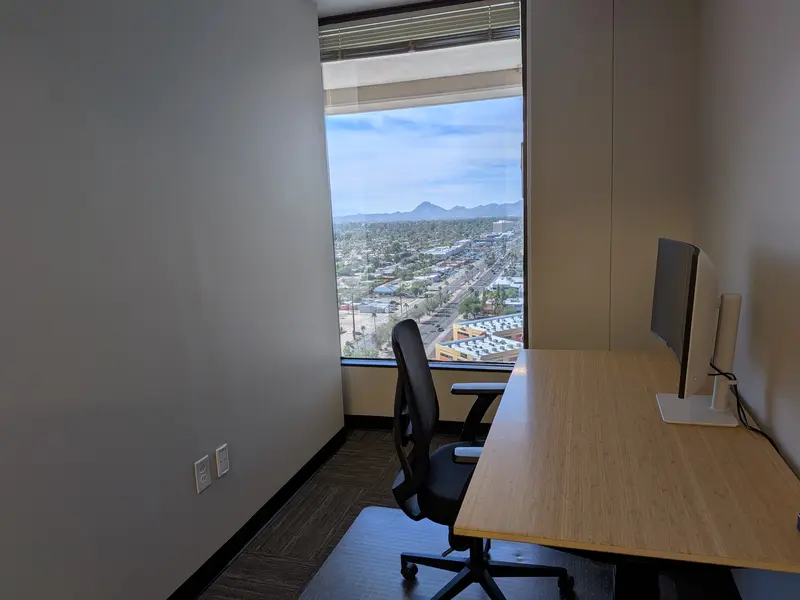 Private office Suite 152 in Tucson featuring a bamboo sit/stand desk, curved monitor, and scenic mountain views.