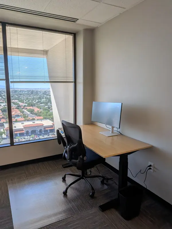 Private office Suite 148 in Tucson with a bamboo sit/stand desk and a window overlooking the city.