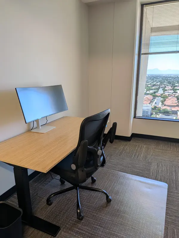 Private office Suite 146 in Tucson featuring an ergonomic bamboo sit-stand desk, curved monitor, and scenic city views.