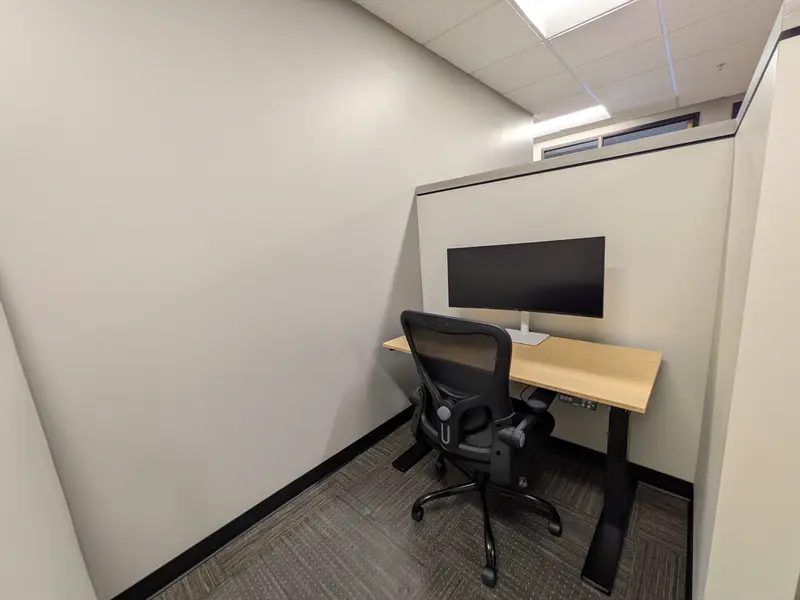 A semi-private dedicated desk 208 with an electric bamboo sit-stand desk, curved monitor, and ergonomic mesh chair.