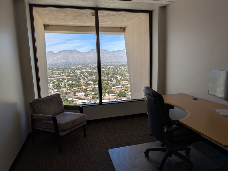 Private executive office Suite 111 featuring a sit-stand desk and a large window with scenic mountain and city views.
