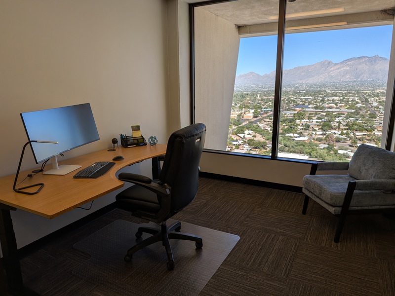 Private executive office Suite 114 with a sit-stand desk, curved monitor, and panoramic mountain views.