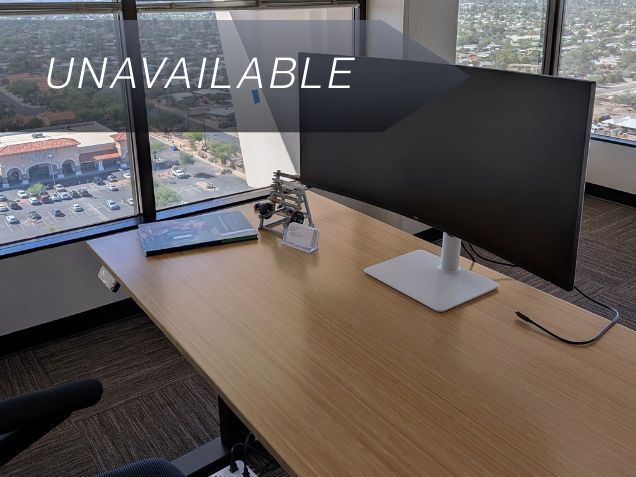 A bamboo sit-stand desk with a 34-inch curved monitor in Suite 149, offering a 17th-floor corner view of Tucson.