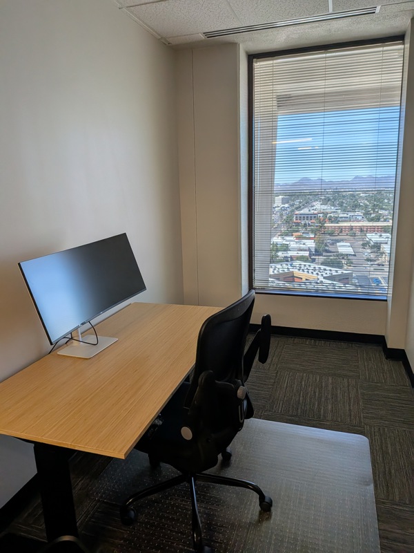 Private office Suite 154 in Tucson featuring a bamboo sit/stand desk, curved monitor, and scenic city views.