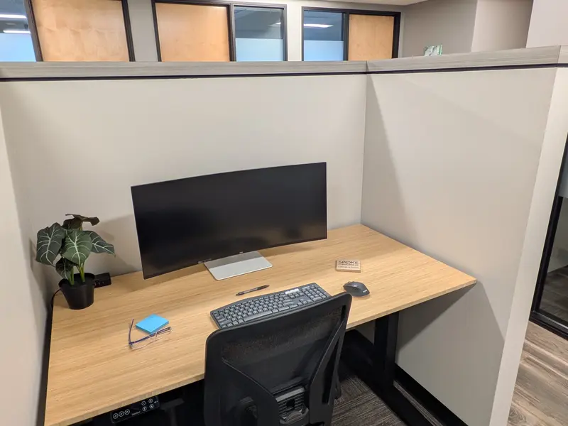 Hot-Desk 202 semi-private workspace with a curved monitor, bamboo sit-stand desk, and ergonomic chair.