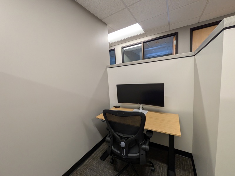 Semi-private dedicated desk 207 with a bamboo sit/stand desk and curved monitor for focused work.