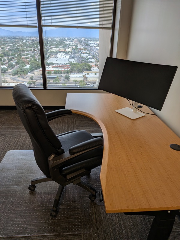 Private executive office Suite 125 with a bamboo sit-stand desk, curved monitor, and scenic city and mountain views.