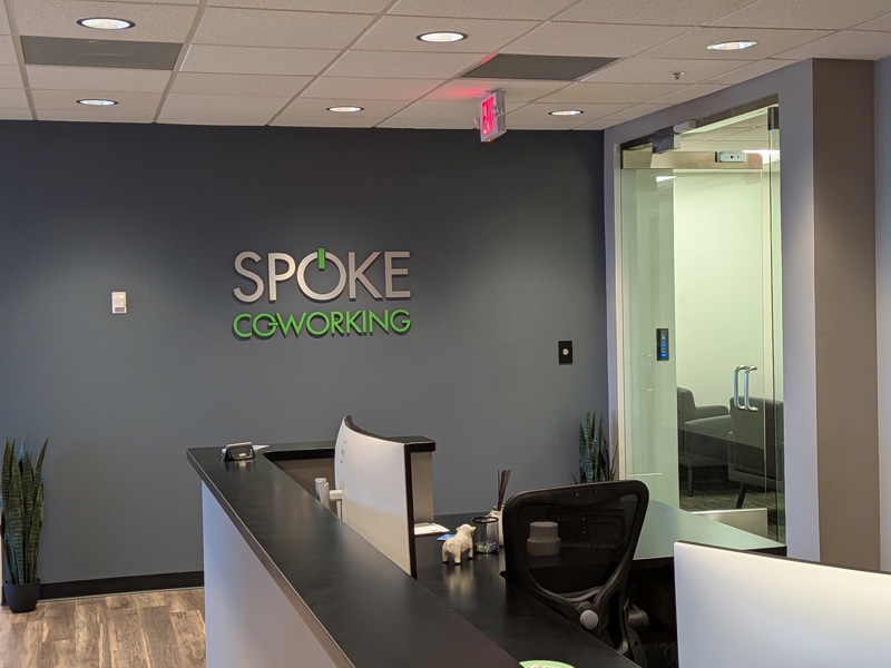 Modern reception desk at Spoke Coworking 5151 featuring a branded wall logo and contemporary office design.