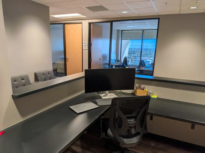 Modern reception desk at Spoke Tower featuring a curved monitor and laptop, with a view of private glass offices.
