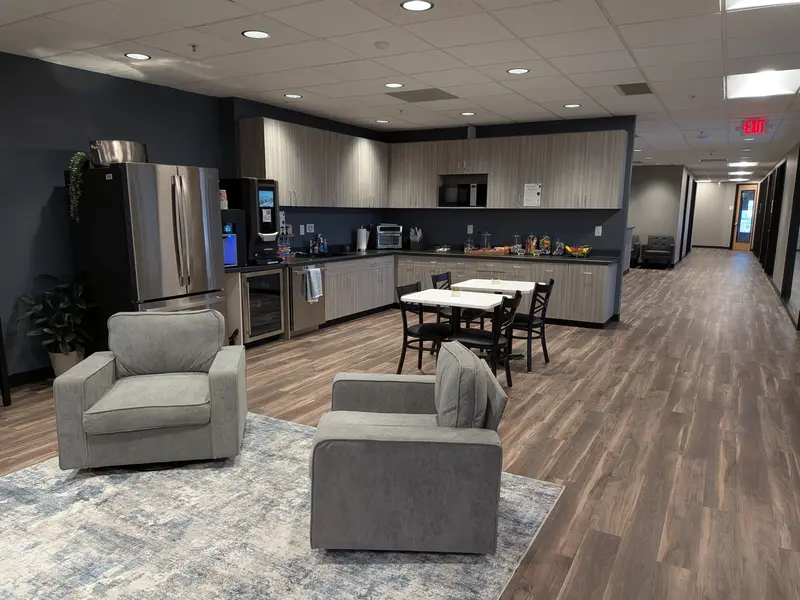 Modern office lounge and kitchenette at Spoke Tower featuring stainless steel appliances, dining tables, and plush armchairs.