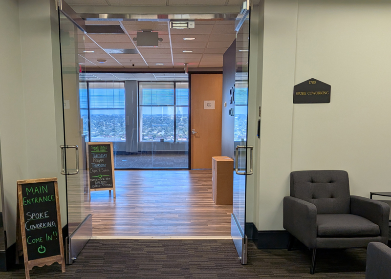 Main entrance to Spoke Coworking at Spoke Tower with open glass doors, a welcome chalkboard, and a scenic city view.