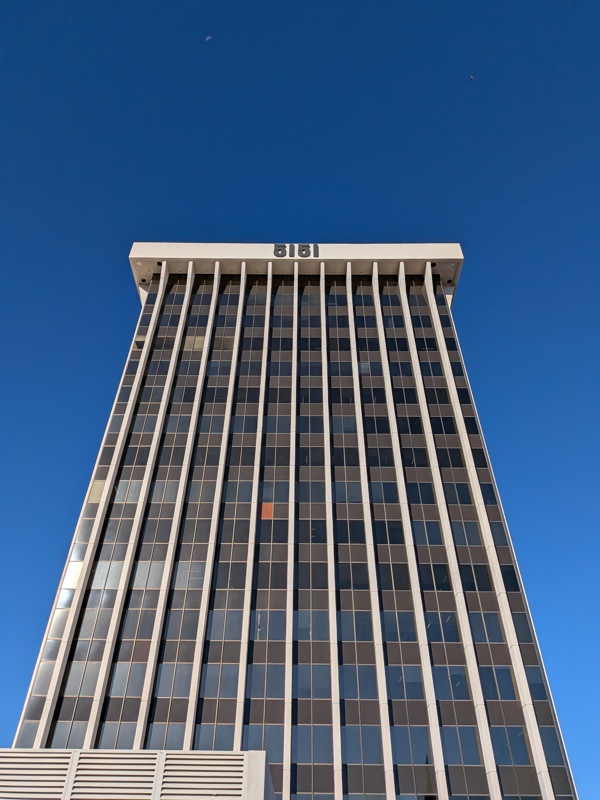 Low-angle view of the 5151 office building's modern grid facade of dark windows and light pillars against a blue sky.