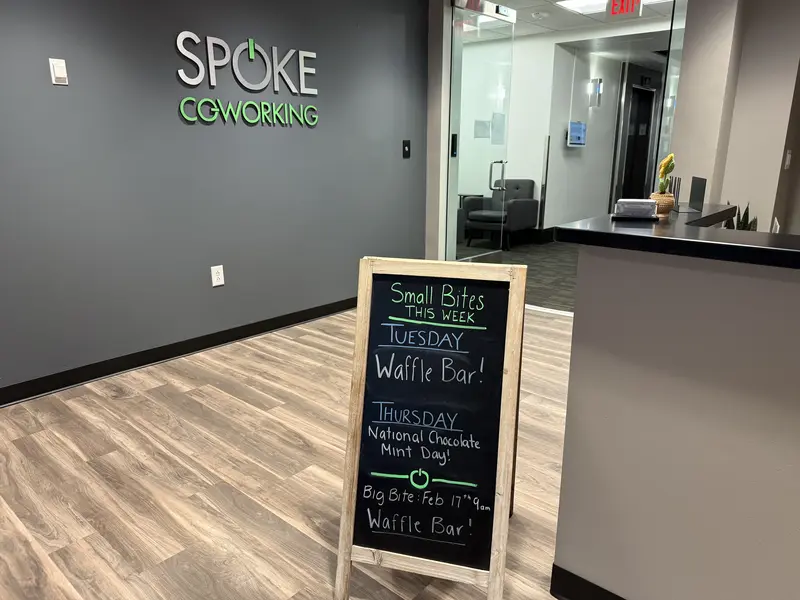 The entrance of Spoke Coworking featuring a branded wall and a chalkboard sign listing weekly community events.