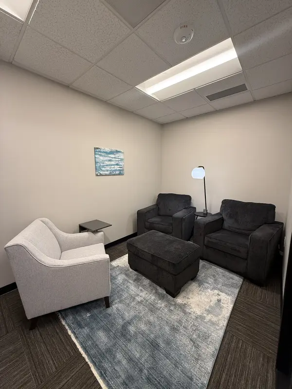 A cozy private meeting room with comfortable armchairs, an ottoman, and a blue rug in a Huddle Hub space.
