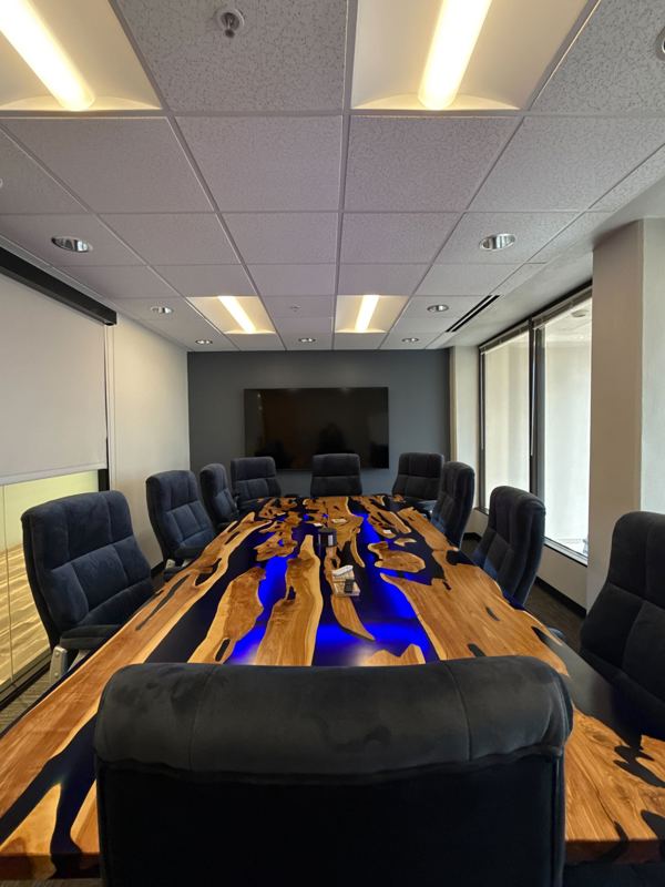 A modern boardroom featuring a unique live-edge wood conference table with a glowing blue resin river inlay.