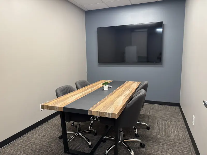 The Think Tank meeting room featuring a wooden conference table, four grey chairs, and a large wall-mounted TV.