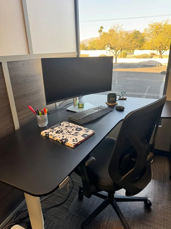 A dedicated office desk with a monitor and ergonomic chair, featuring a window view of the outdoors.