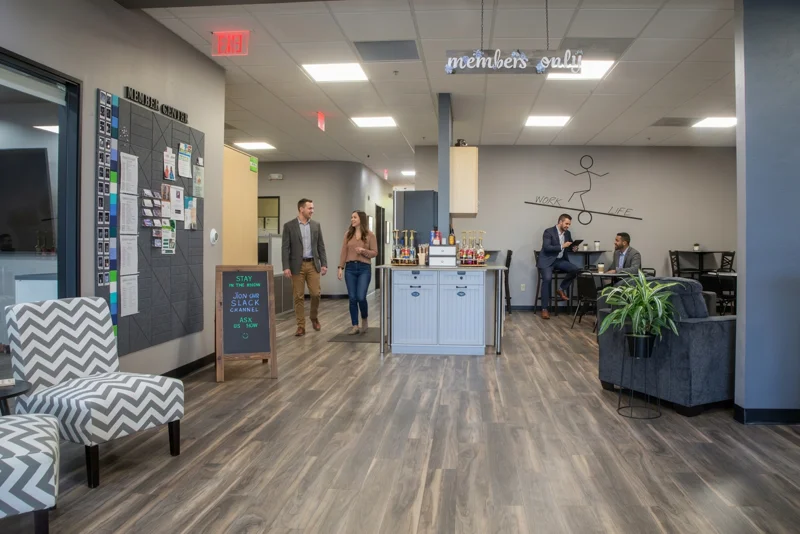 Modern coworking space lounge with a member center bulletin board, coffee station, and work-life balance wall graphic.