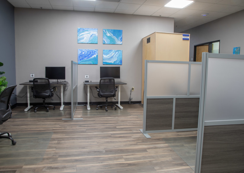 Modern coworking space featuring two hot desk workstations with monitors, ergonomic chairs, and privacy screens.