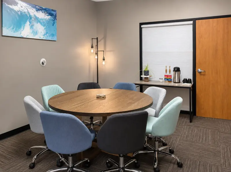 The Conference Lounge meeting room featuring a round wooden table, comfy chairs, and coffee station in East Tucson.