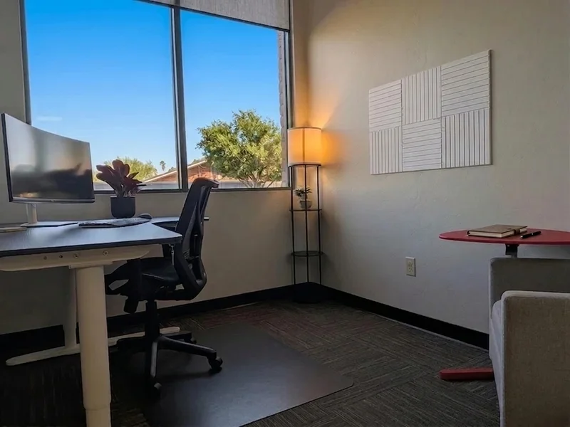Private office suite at Spoke Coworking in East Tucson with a sit-stand desk, curved monitor, and comfortable armchair.