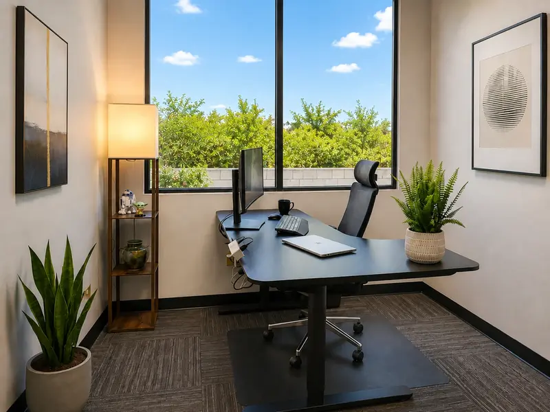Private office Suite 123 at Spoke Coworking with an ergonomic sit-stand desk, curved monitor, and large sunny window.