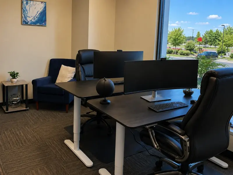 Private Suite 102 at Spoke Coworking HQ with electric sit-stand desks, curved monitors, and natural window light.