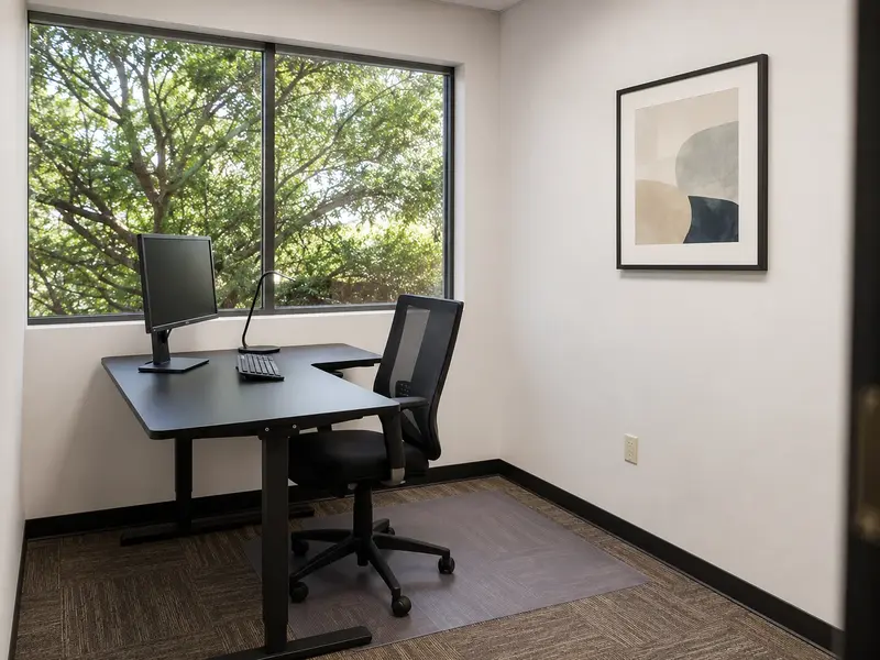 Private office Suite 119 at Spoke Coworking with an ergonomic sit-stand desk and large window view of trees.